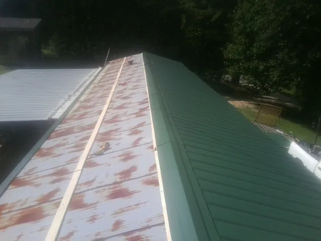 Old rusted panels beside newly installed green metal roofing — Wind Damage Roof Repair by Roofing Brothers in Homestead