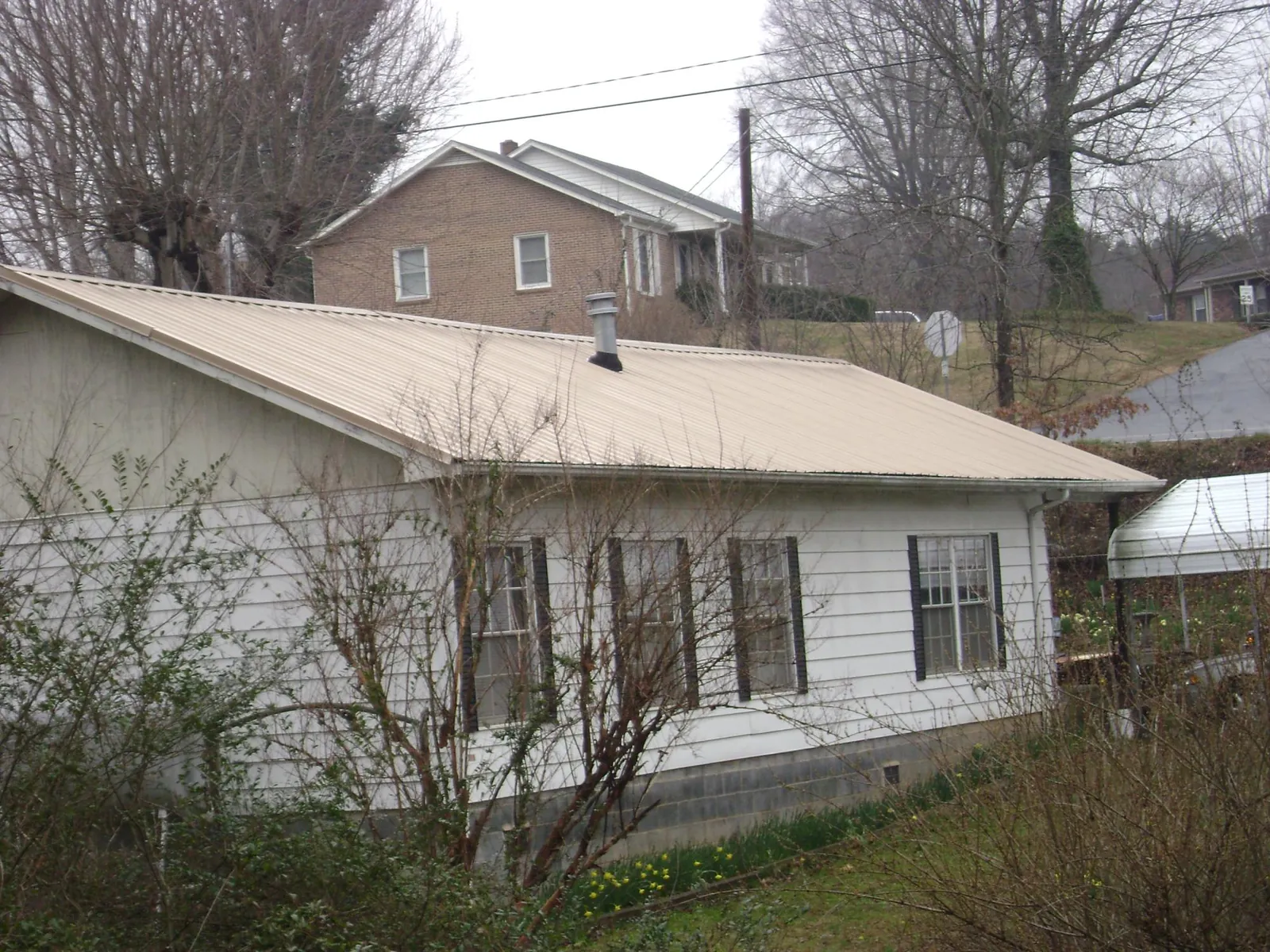 Tan metal roof on a white sided house set into a hillside — Commercial Roofing by Roofing Brothers in Homestead